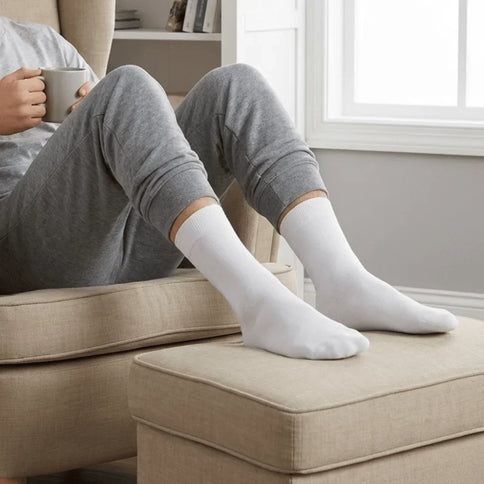 Persoon in grijze joggingbroek met witte Hipperboo bamboesokken op een poef.