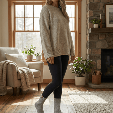 Vrouw in beige trui en zwarte leggings met Sukats® grijze sokken in een woonkamer.