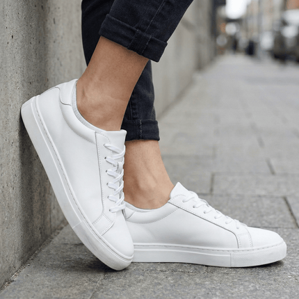 Witte sneakers gedragen met Sukats sneakersokken op een stenen stoep.