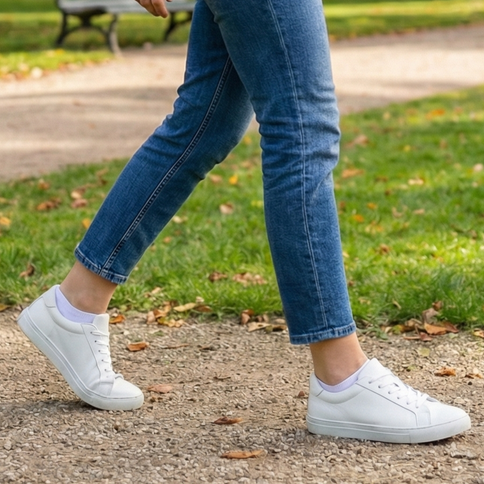 Persoon draagt witte sneakers met Sukats sneakersokken en een blauwe jeans.