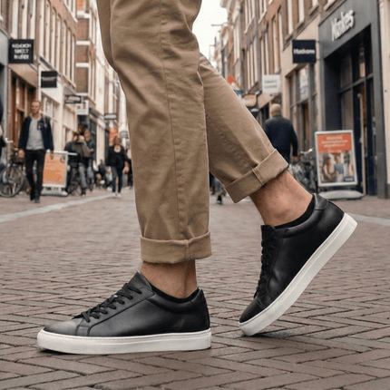 Man met zwarte Sukats sneakersokken en zwarte leren sneakers op een stenen straat.