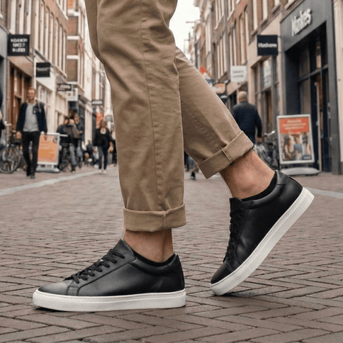 Man met zwarte Sukats sneakersokken en zwarte leren sneakers op een stenen straat.