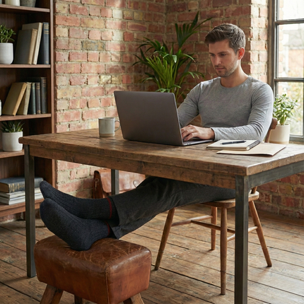 Man met Sukats Noorse sokken zittend aan een houten bureau met laptop.